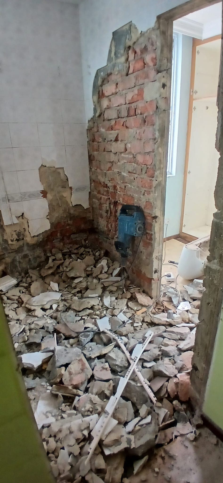 Breaker tool beside exposed brick wall and hacking debris